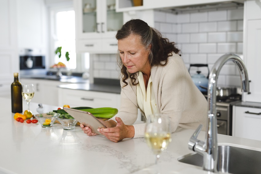 Senior caucasian woman in modern kitchen, using tablet computer. retirement lifestyle, spending time at home. Senior woman researching herbal recipes